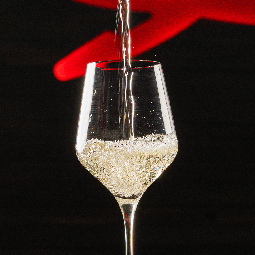 Sparkling wine being poured into a wine glass standing against a black background.