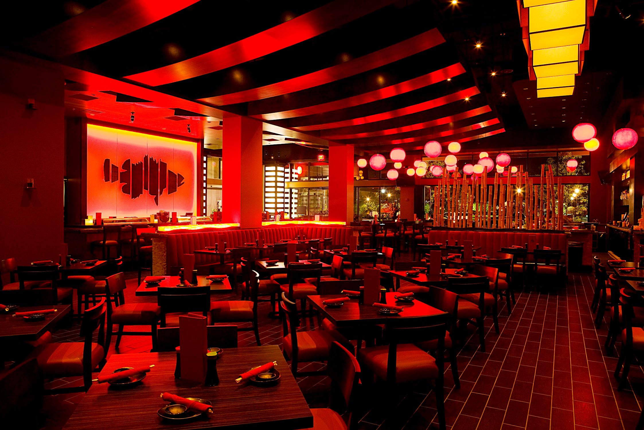 Interior Shot showing red accent lighting and circular wooden tables and chairs. Along with an image of a fish on the wall to the left